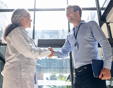 Young male doctor shakes hands with senior female doctor in hospital lobby. 