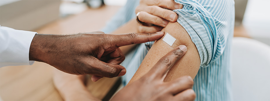 A doctor places a bandage on the arm of a patient after administering a vaccine shot.