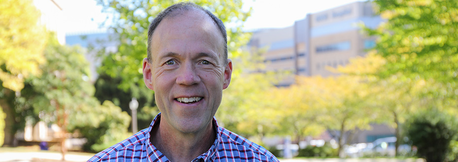 Portrait of Dr. Kevin Duff on the Marquam Hill lawn with OHSU Hospital in the background.