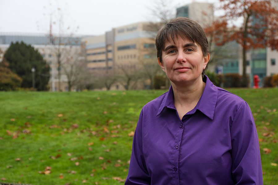 Dr. Nathalie Huguet standing outside on Marquam Hill with OHSU campus visible behind her.