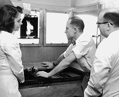 Old black and white photo shows Dr. Charles Dotter and Dr. Herbert Griswold reviewing a heart X-ray held up by X-ray technician, Kay Smith, circa 1955.