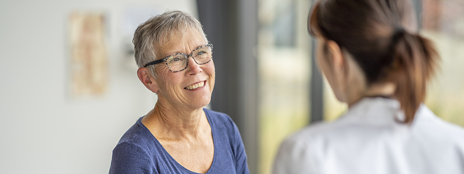 A senior woman wearing glasses talks with a doctor in a hospital room.