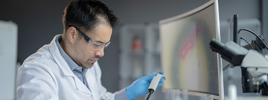 A male scientist in a lab injects liquid into test tubes to analyze.