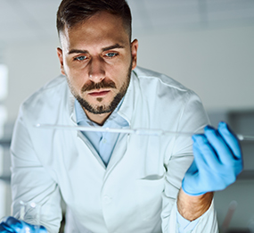 A male doctor in a laboratory examines liquid inside a clear tube.