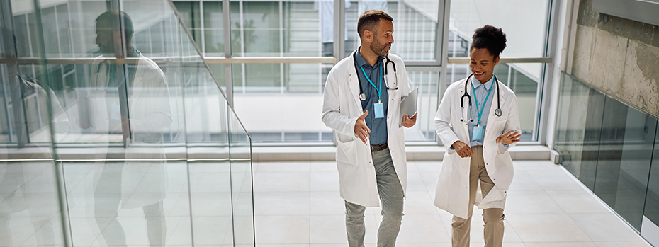  A male and a female doctor smile and talk as they walk up a stairway inside a building.
