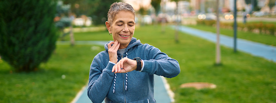  A senior woman checks her pulse and smartwatch during a jogging workout.