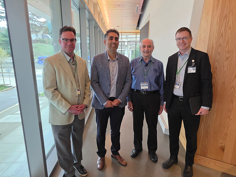 A group of four men in professional attire pose for a photo in bright hallway.