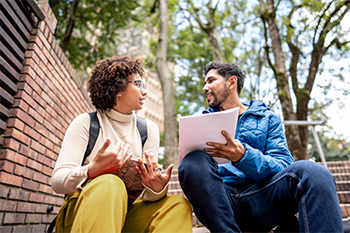 Two OHSU students sitting outside on steps having a conversation.
