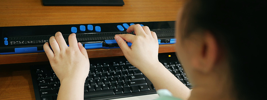 A person accesses a computer using an assistive device with braille.