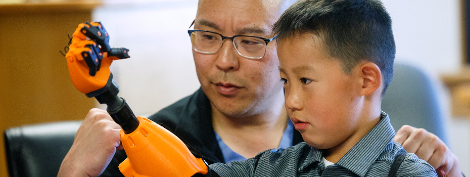 Dr. Albert Chi, a professor of surgery at OHSU, assists patient Jude Rochon with his 3D prosthetic hand.