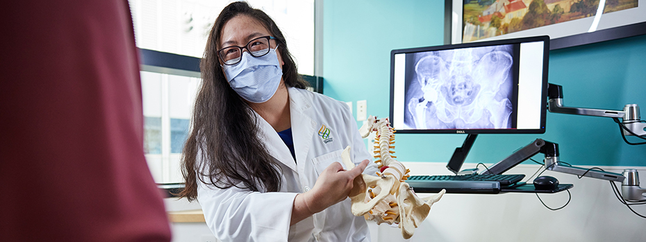 An OHSU doctor shows a patient a model of a human pelvis and lower spine.