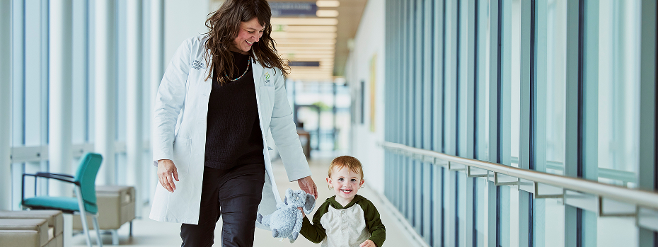 Dr. Lori Howell, a plastic and reconstructive surgeon at OHSU, walks and smiles with a young patient along a well-lit hallway.