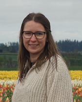 A woman stands smiling in front of a field of different colored flowers on a cloudy day.
