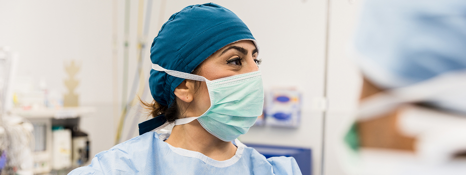A female surgeon wearing a mask gives direction to a colleague during an operation.