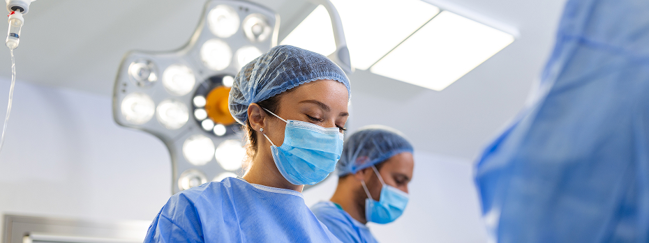 A young female surgeon in an operating room wearing a mask performs a medical procedure with colleagues.