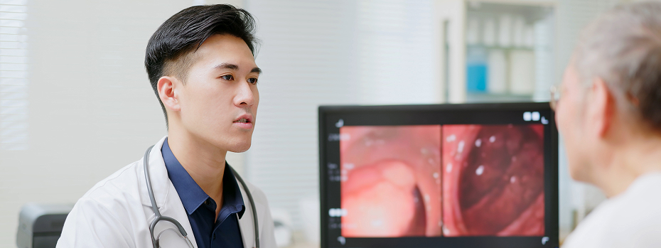 A male doctor explains to an older adult the colonoscopy tumor surgery result shown on a computer screen.
