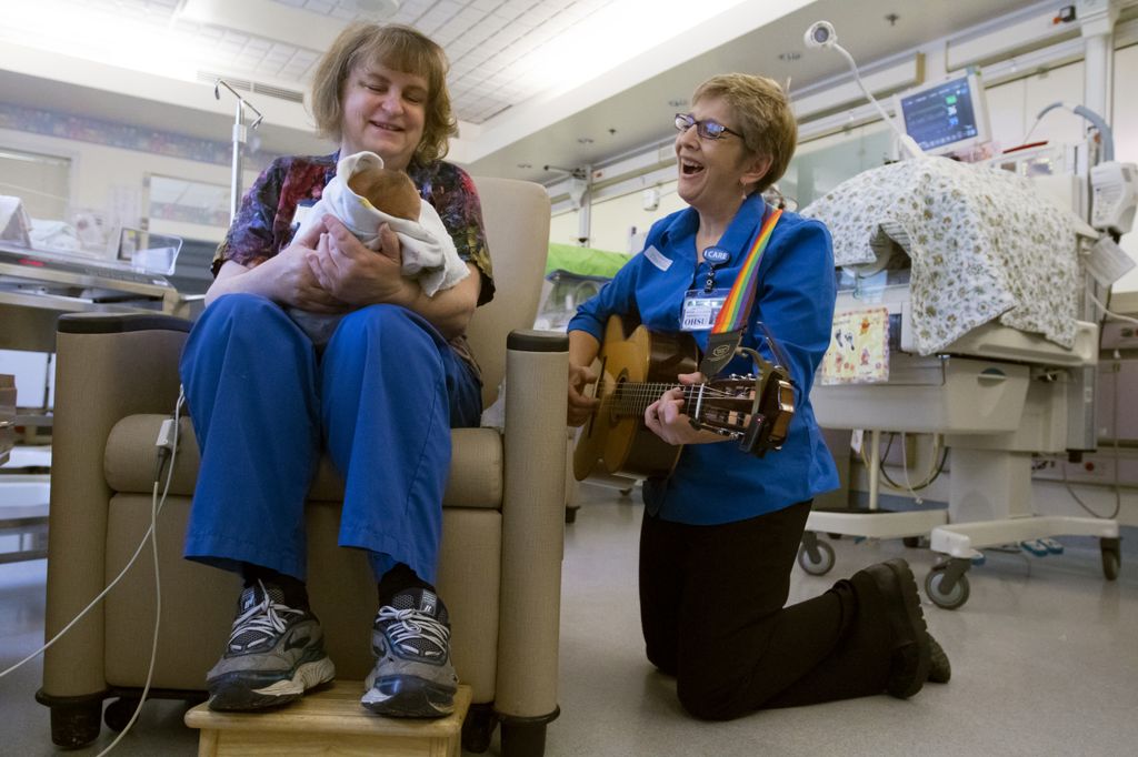 A volunteer plays guitar to a baby being held. 