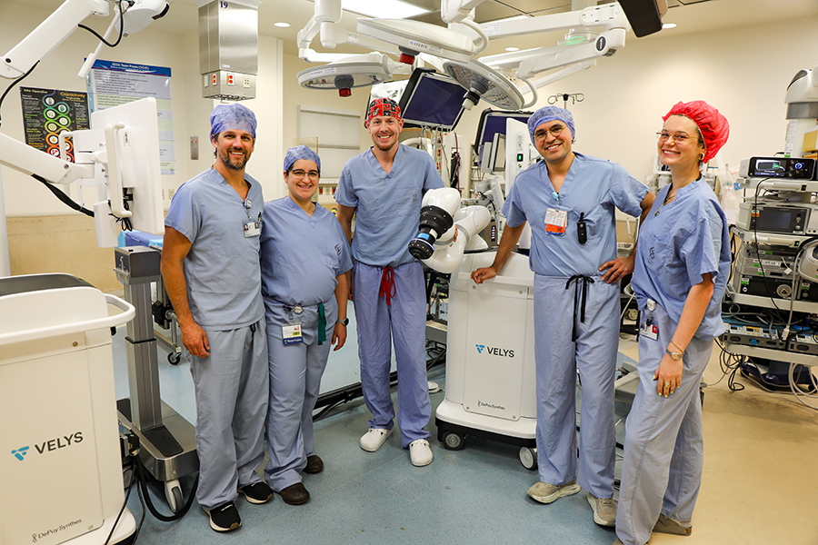 Three men and two women, all wearing hospital scrubs, stand next to each other smiling in an operating room.