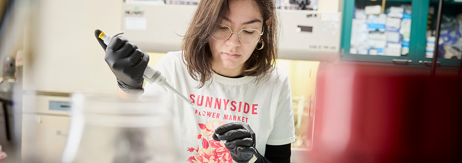 Giselle Jimenez wears black gloves and uses her thumb to push down the plunger of a long syringe.