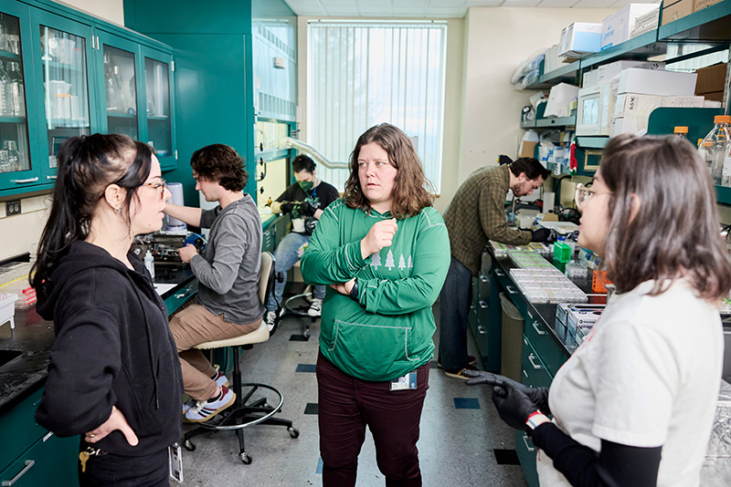 Dr. Nora Gray and two members of her team talk in the foreground. In the background, three other team members work with brain tissue samples in specimen trays and microscope slides.