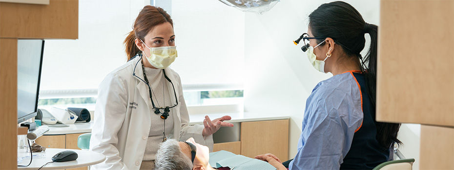 A professor and dental student talk as they examine a patient.