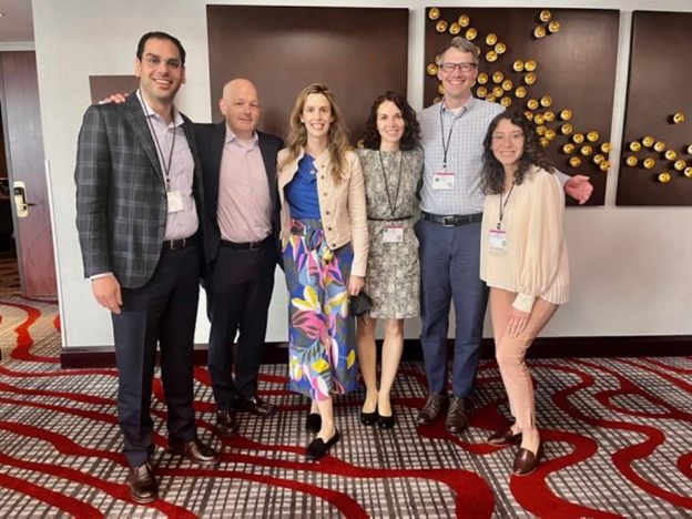 A group of OHSU Adult Congenital Heart Disease (ACHD) faculty and fellows pose for a group photo in a hotel lobby at a conference.