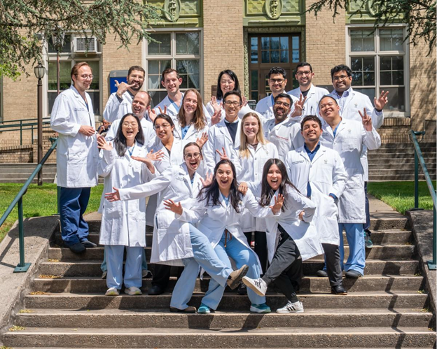 A large group of cardiovascular disease fellows wearing white coats pose for a funny photo on steps outside OHSU.