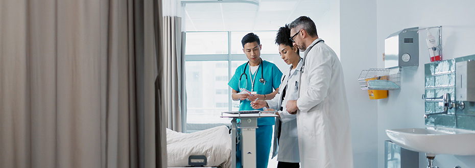 A group of faculty and fellows consult a patient’s chart at the end of a hospital bed.