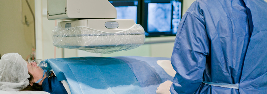 A doctor performs a procedure on a patient in a cath lab in a hospital.