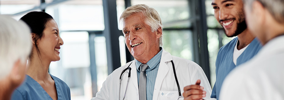 An older male doctor speaks to his younger colleagues at a hospital.