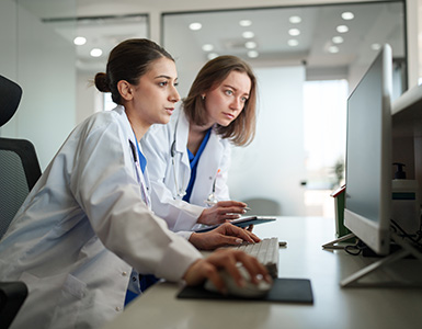 Two female doctors work together at a computer reviewing documents.