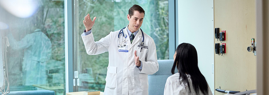 A male doctor speaks to a female patient in a hospital room.