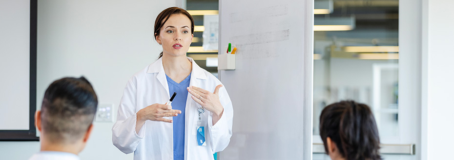 A young female doctor makes a presentation in front of other doctors in a medical building.