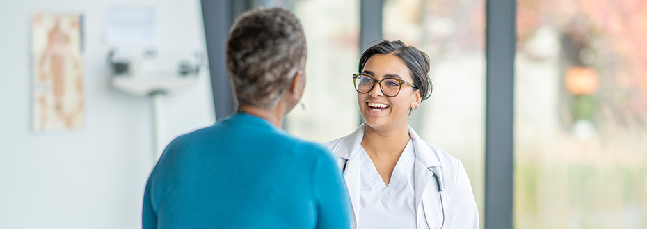 A young female doctor speaks with an older female patient in an exam room.