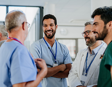 A young male doctor speaks with an older male colleague in a hospital.