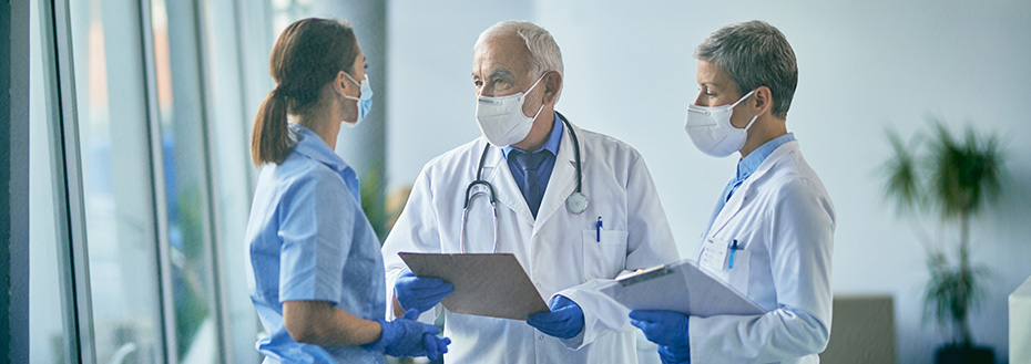 A team of medical experts wearing masks talk while going through medical reports in hallway at a hospital.