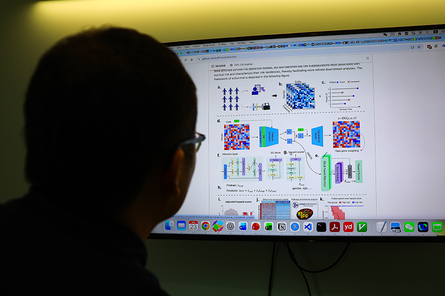 A man looks at a large computer monitor in a dark room.