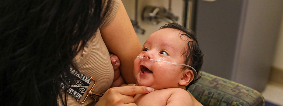 A baby beams at his mother as she holds him.