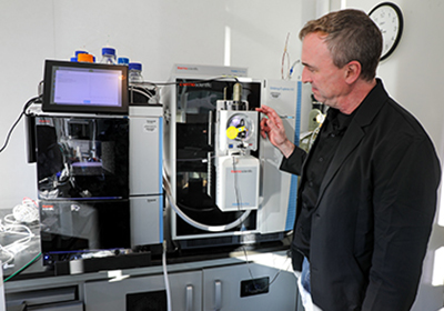An OHSU scientist stands next to a liquid chromatography-mass spectrometry system.
