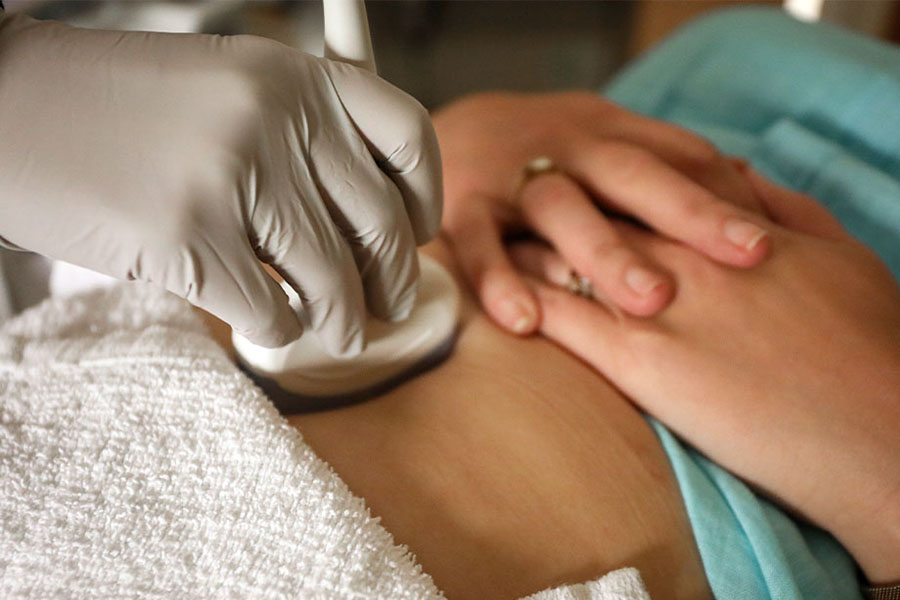 A gloved hand holds an ultrasound instrument over a woman's stomach.