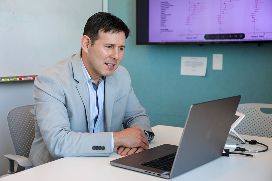 A man sitting at a conference room table looking at a laptop screen.
