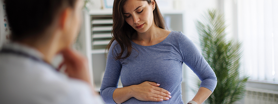 A woman places a hand on her pregnant belly at a doctor visit.