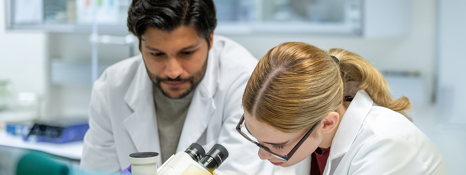 Two young lab scientists work together near a microscope in a laboratory.