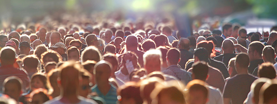 A crowd of people walks outside in sunshine.