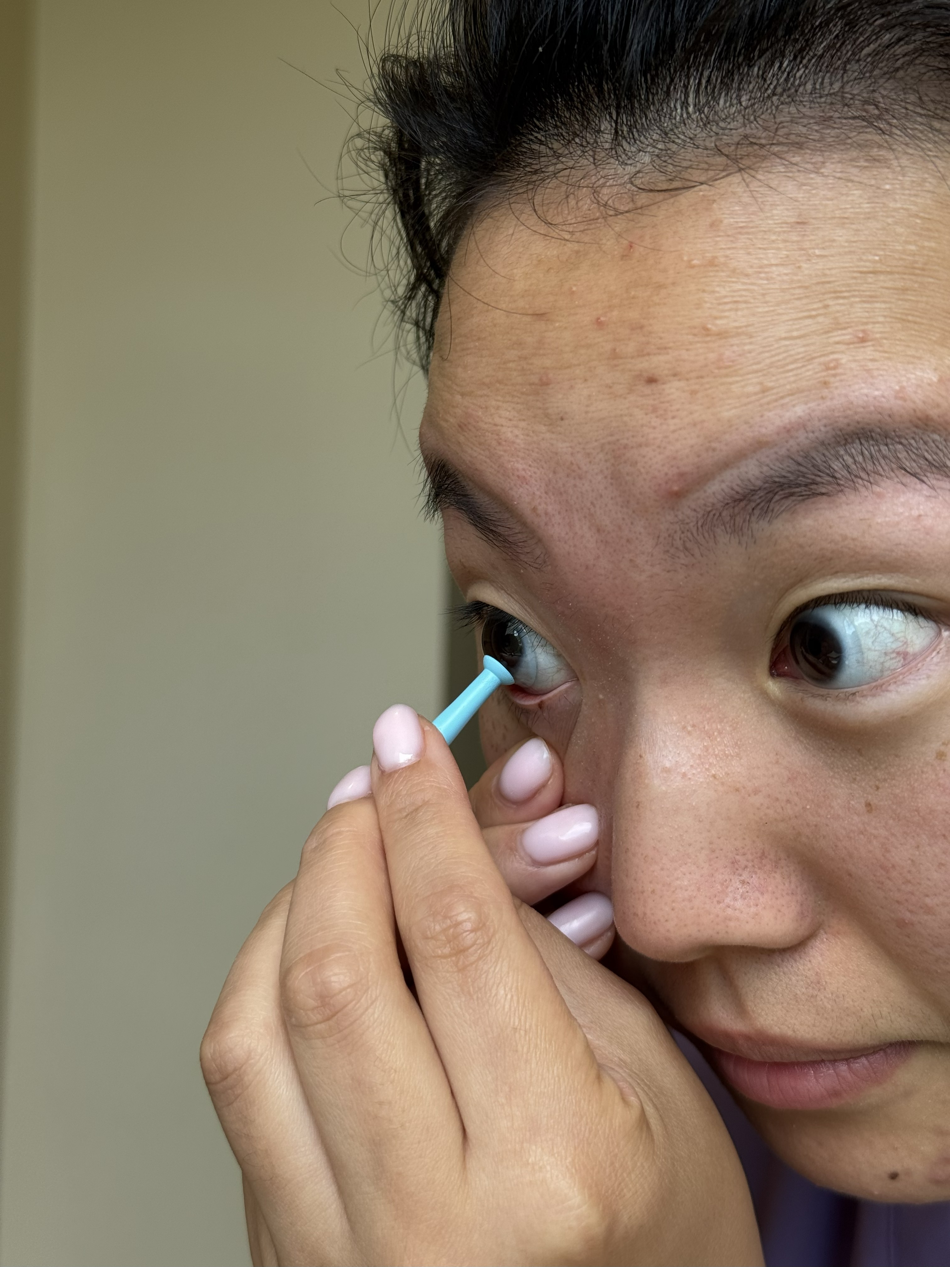 A close up of a woman's face as she puts a blue contact lens removal tool on top of her contact lens in her eye.