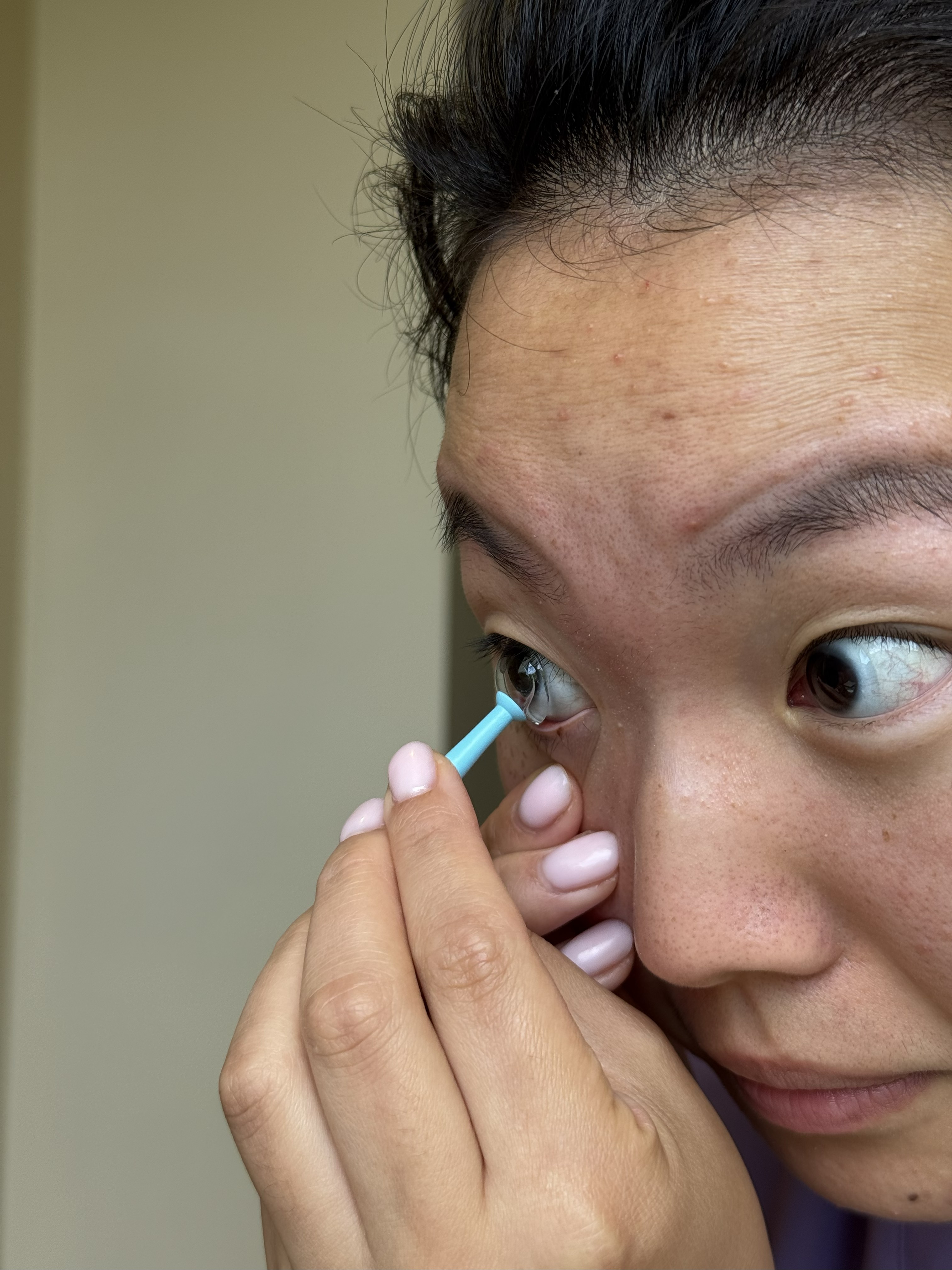 A close up of a woman's face as she pulls a contact lens out of her eye with a blue contact lens removal tool.
