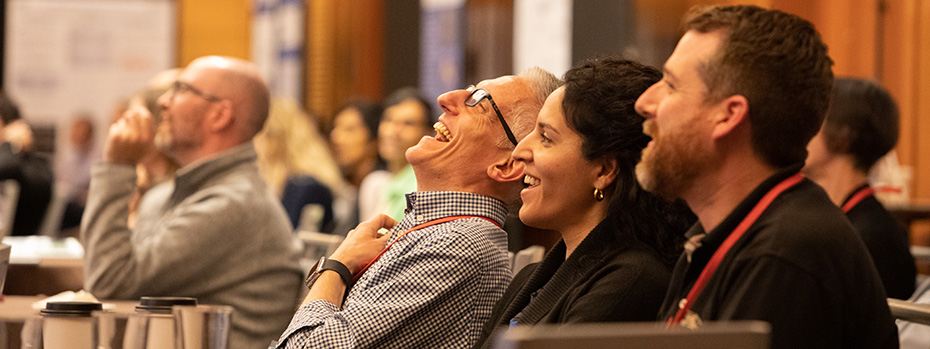 Conference attendees smiling and laughing during a presentation.