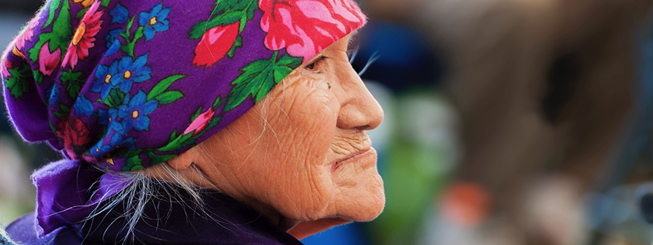 An older Indigenous woman wearing a scarf around her head looks into the distance.