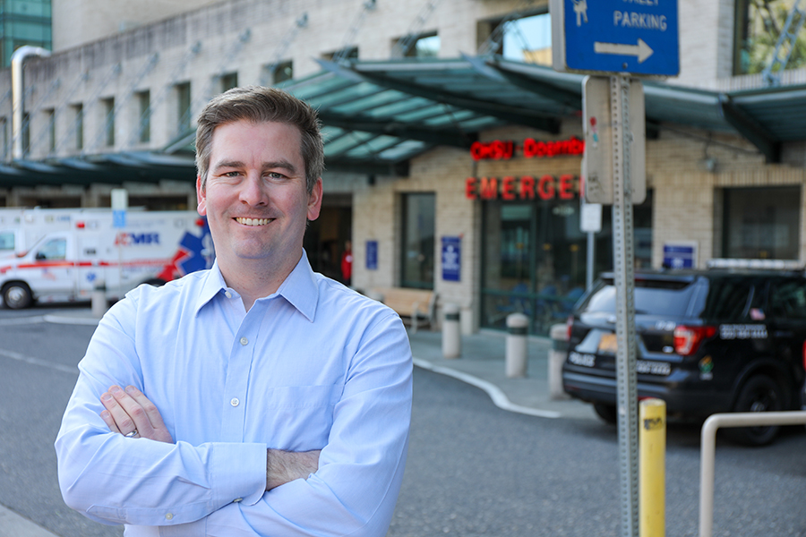 A man stands with his arms crossed smiling in front of the OHSU Doernbecher Emergency Room entrance.