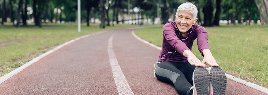 A senior woman in athletic wear stretches to touch her toes on a running track.